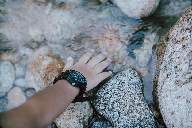 Main coupée d'une personne touchant une roche dans un ruisseau