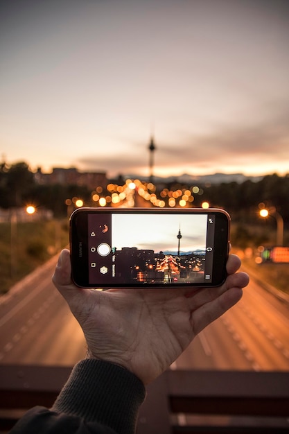 La main coupée photographie la tour dans la ville à partir d'un téléphone portable au crépuscule.