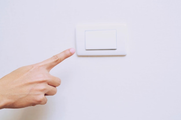 Photo main coupée pointant vers l'interrupteur sur le mur blanc