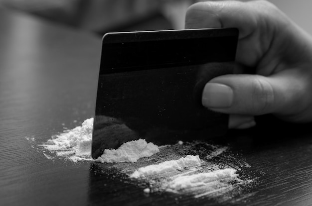 Photo une main coupée qui prend de la cocaïne avec une carte de crédit sur la table.