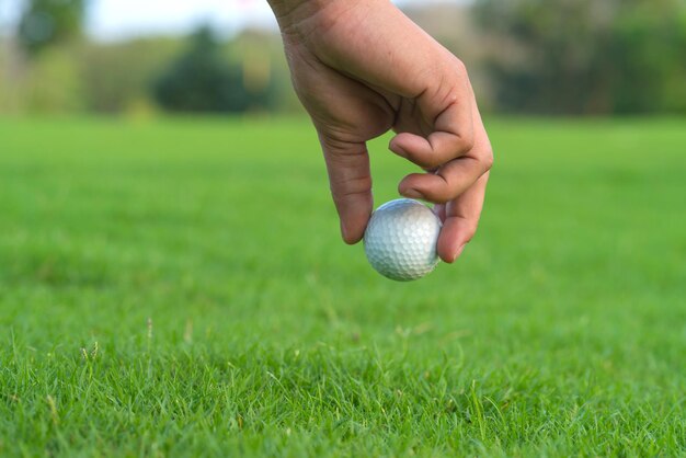 Photo main coupée tenant une balle de golf sur l'herbe