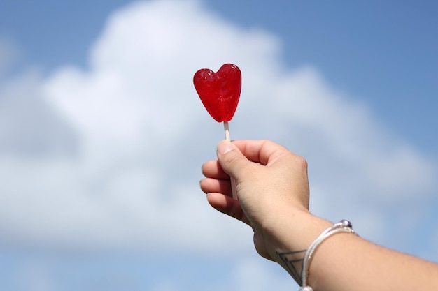 La main coupée tenant des bonbons en forme de cœur contre le ciel