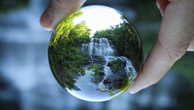 Main coupée tenant une boule de cristal avec une réflexion de cascade