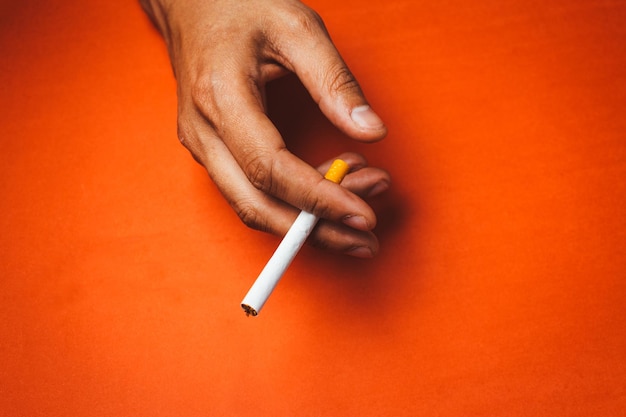 Main coupée tenant une cigarette sur un fond orange