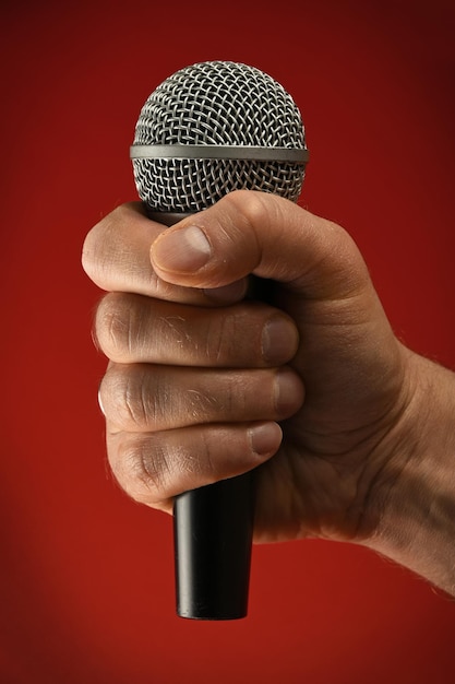 Main coupée tenant un microphone sur un fond rouge