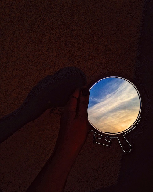 Main coupée tenant un miroir avec le reflet du ciel dans la chambre noire