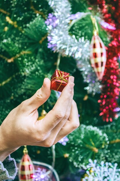 Photo main coupée tenant un petit cadeau de noël par l'arbre