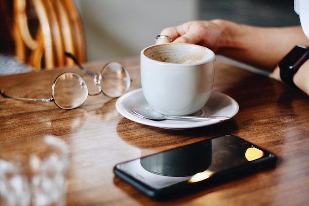 Main coupée tenant une tasse de café par téléphone intelligent sur la table
