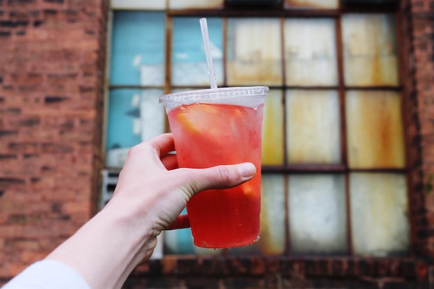 La main coupée tenant un verre de cocktail contre la fenêtre