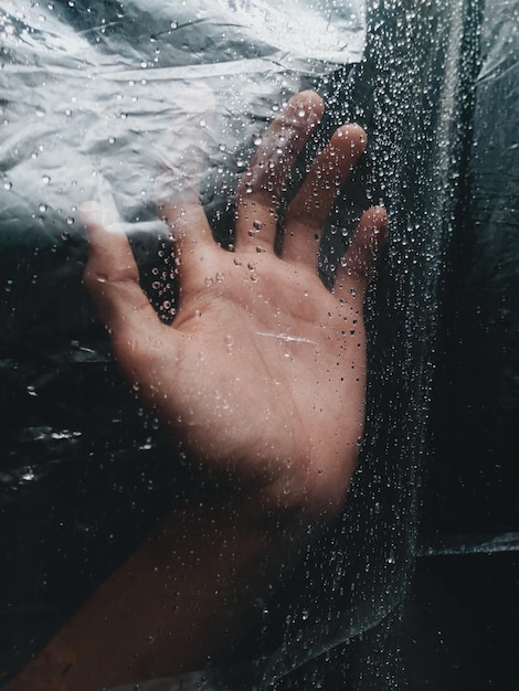 La main coupée touchant du plastique mouillé pendant la saison des pluies