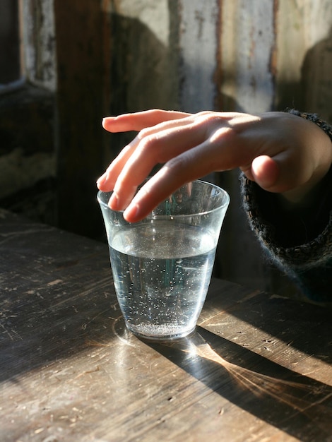 Une main coupée touchant un verre à boire sur une table en bois