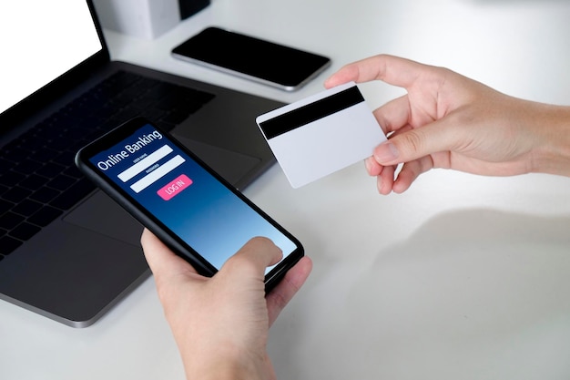 Main coupée en utilisant le téléphone tout en tenant une carte de crédit par ordinateur portable sur la table