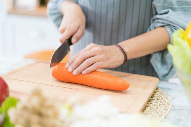 Main avec un couteau coupe carotte. Femme prépare la nourriture à table.