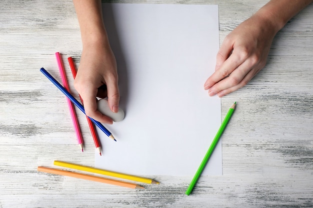 Main avec des crayons de couleur et une feuille de papier vierge sur une table en bois