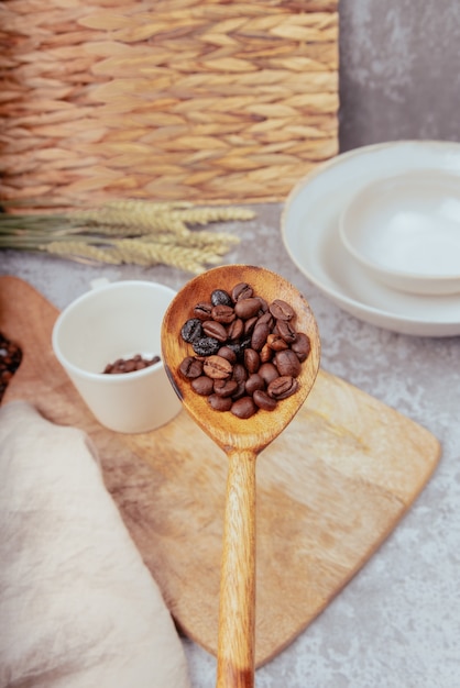 Main avec une cuillère en bois versant des grains de café dans une tasse en céramique blanche