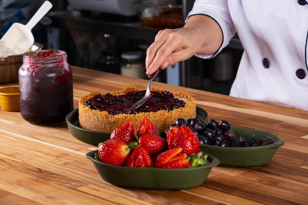 main avec cuillère répandant de la confiture de baies sur une tarte sucrée