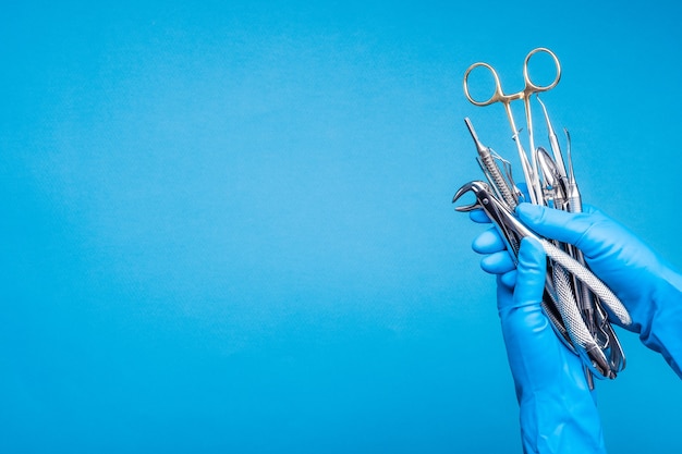 Main dans un gant bleu tenant des outils dentaires de chirurgie sur fond bleu clair