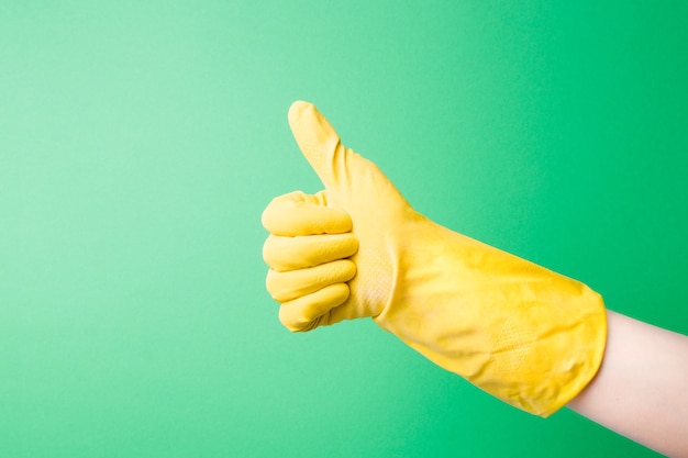 La main dans un gant en caoutchouc jaune montre le geste du pouce vers le haut