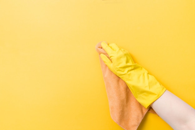 La main dans un gant en caoutchouc jaune tient un chiffon orange pour le lavage et le nettoyage