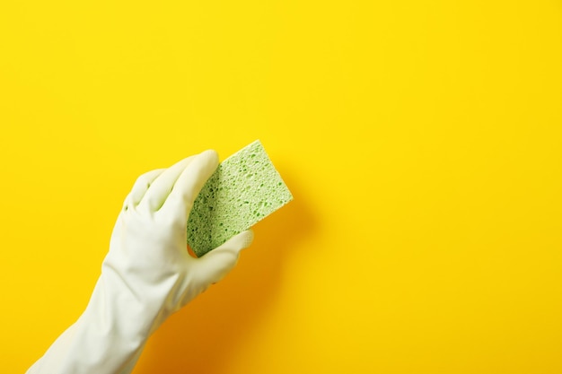 Photo une main dans un gant en caoutchouc vert tient une éponge de lavage sur fond jaune