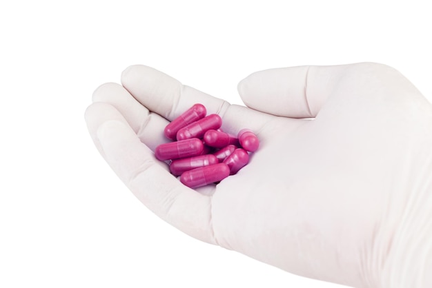 Main dans un gant médical tenant des capsules de médecine bio de couleur rose en plastique isolées sur fond blanc gros plan
