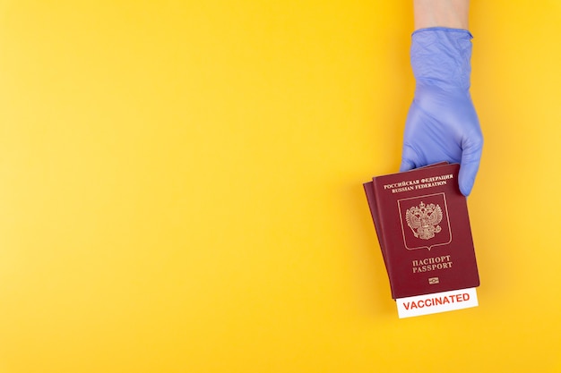 Main dans un gant médical tenant un passeport avec timbre vacciné sur fond jaune