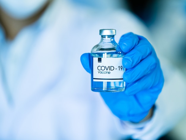 Main dans des gants bleus médicaux tenant une bouteille de vaccin contre le coronavirus COVID-19.