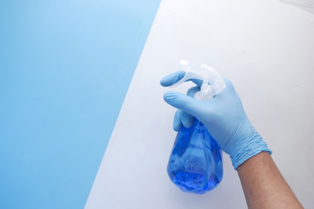 Main dans des gants en caoutchouc bleu tenant un flacon pulvérisateur avec espace de copie