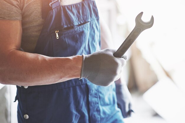 Photo la main dans des gants avec une clé métallique sur le fond d'une usine de costumes de travailleurs