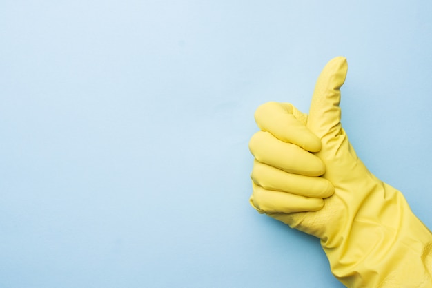 La main dans des gants jaunes pour le nettoyage sur fond bleu.