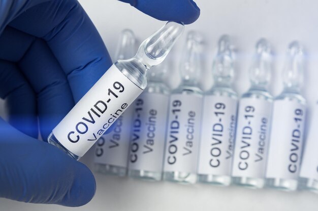 Main dans des gants en latex tenant un flacon avec étiquette Covid19 Coronavirus vaccin