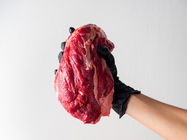 Une main dans des gants noirs tient des morceaux de viande crue fraîche sur fond clair