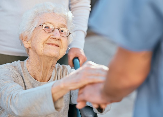 Main dans la main soignant et femme âgée en fauteuil roulant pour un soutien en plein air dans une maison de retraite Amour confiance et infirmière en soins de santé ou médecin en bien-être médical pour patient handicapé avec gentillesse