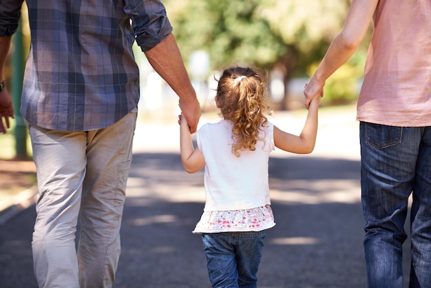 Main dans la main à travers l'enfance Vue arrière d'une jeune famille marchant dans la rue