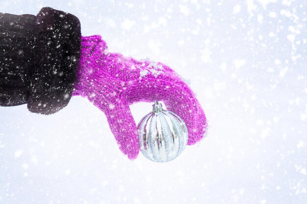 Main dans une moufle tenant une boule de Noël sur fond blanc Joyeux Noël et bonne année