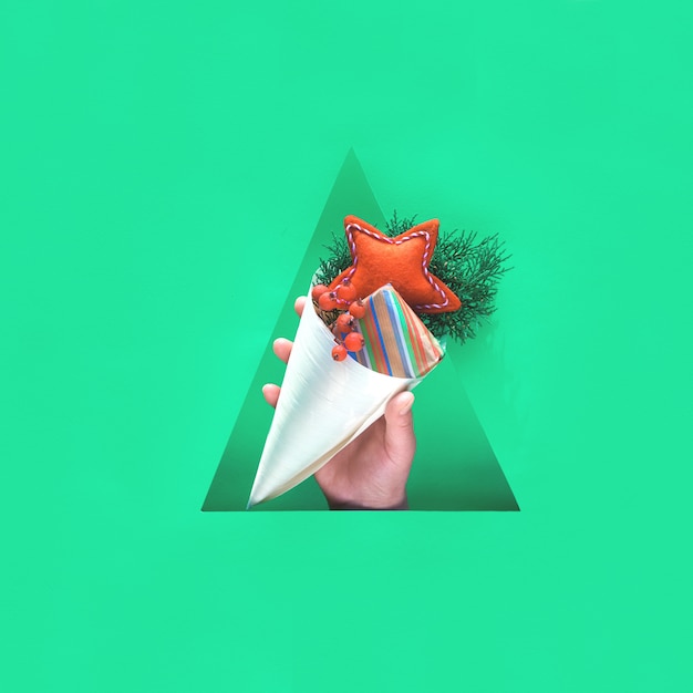 Main avec des décorations naturelles, coffret cadeau en papier kraft et étoile rouge fait main en feutre doux en cône de contreplaqué dans un trou de papier triangulaire. Joyeuses vacances d'hiver zéro déchet