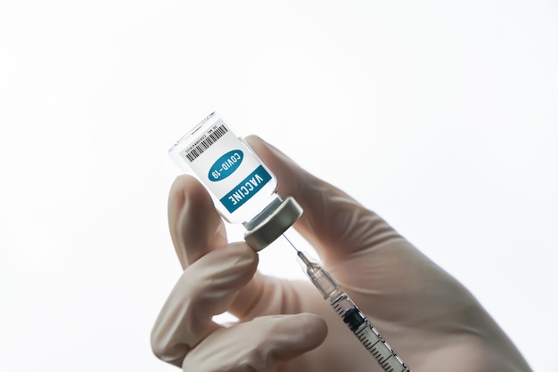 Main de docteur tenant le vaccin contre le coronavirus dans une bouteille en verre et une seringue sur fond blanc