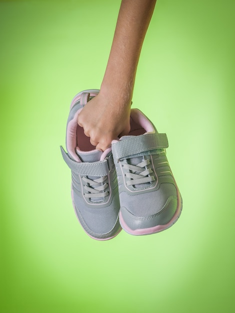 La main droite de l'enfant tient des baskets pour femmes à la mode sur fond vert. Chaussures de sport. Tendance de couleur.