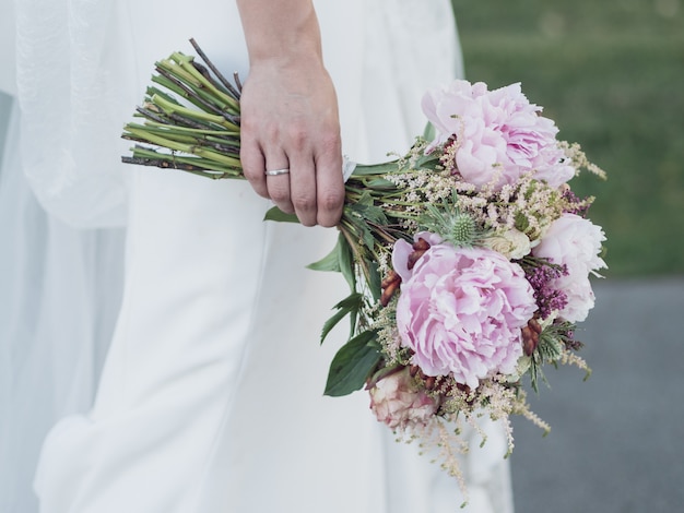 Main droite d'une mariée tenant les bouquets de fleurs sur sa robe