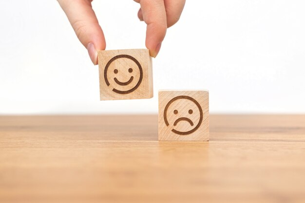 La main du client choisit l'icône du visage souriant sur un cube en bois. Note de service, satisfaction et photo de concept marketing