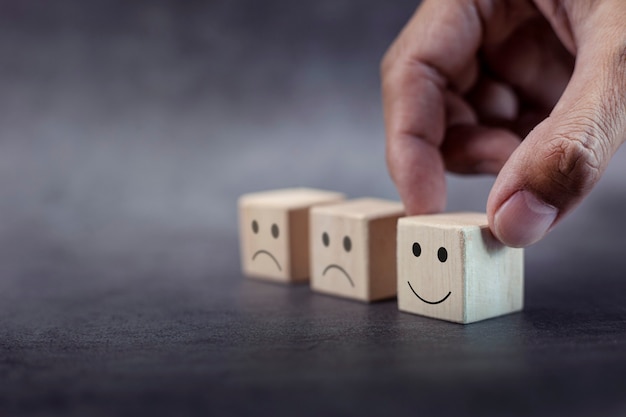 La main du client choisit le visage souriant et le visage triste flou sur un cube en bois