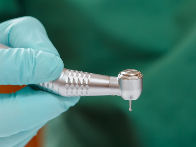 La main du dentiste dans un gant en latex menthe avec une nouvelle pièce à main dentaire à grande vitesse sur l'arrière-plan flou. Concept d'outils médicaux.