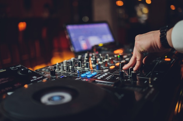 La main du DJ sur l'ordinateur portable et la console de mixage contrôlant les paramètres sonores.