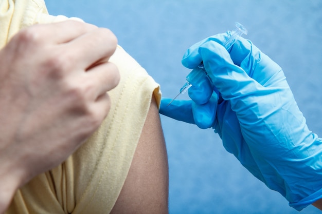 Main du docteur dans le gant bleu tenant la seringue pour la vaccination au bras supérieur du patient. Prévention de la grippe. Mise au point sélective sur la seringue