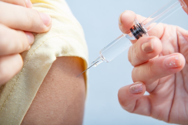 Main du docteur tenant la seringue pour la vaccination au bras supérieur du patient pour la prévention de la grippe.