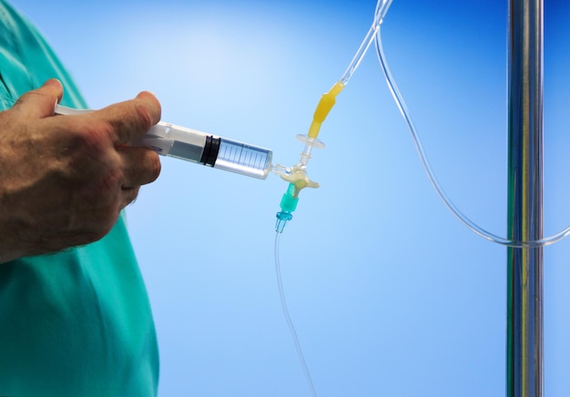 La main du médecin anesthésiste injecte le médicament à travers une seringue au compte-gouttes médical à l'hôpital sur fond bleu