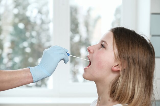 La main du médecin avec un coton-tige prend une analyse de la bouche d'une fille.