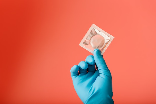 La main du médecin dans un gant bleu contient un préservatif dans un emballage. Latex de sperme et protection contre la grossesse.