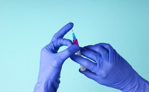 La main du médecin dans des gants en latex tient une seringue contenant un vaccin. Vaccination