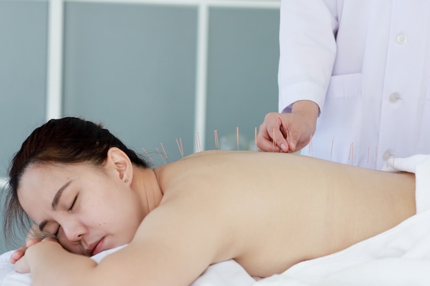 Main du médecin effectuant un traitement d'acupuncture. Femme asiatique subissant un traitement d'acupuncture avec une ligne d'aiguilles fines insérées dans la peau de son corps à l'hôpital clinique